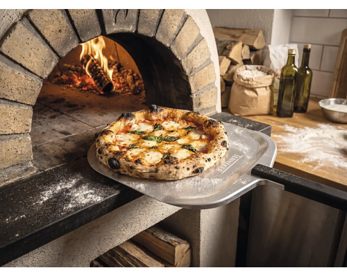 Čerstvě upečená pizza na lopatě na pizzu s Tenneker Logo před hořící kamennou pecí v rustikální kuchyni.