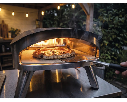Venkovní nerezová pec na pizzu s hořícími plameny a pizzou na pizzovém kameni, s níž se manipuluje pomocí lopaty na pizzu.