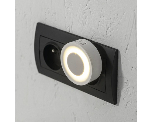 Kulaté bílé noční LED světlo se senzorem do zásuvky, zapojené do nástěnné zásuvky.