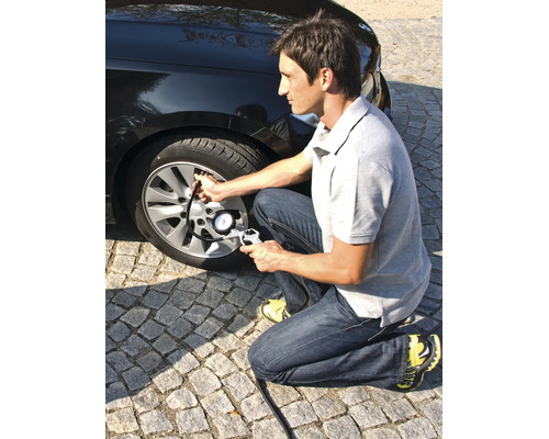 Muž kontroluje tlak v pneumatikách automobilu pomocí pneuhustiče s manometrem.