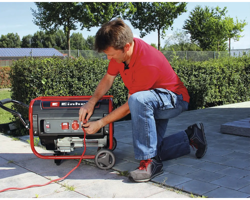 Muž klečí na terase a zapojuje kabel do mobilní elektrocentrály Einhell.