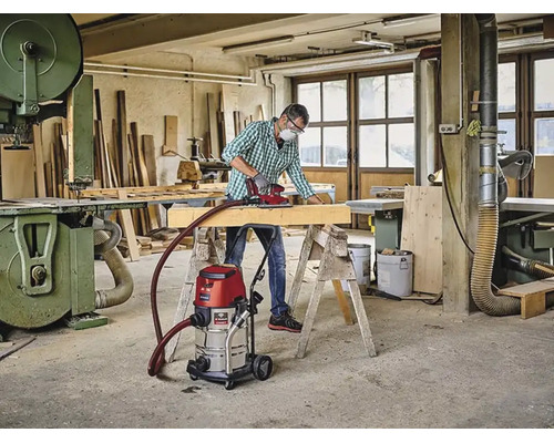 Řemeslník brousí dřevěný trám v dílně pomocí vysavače na mokré a suché sání Einhell připojeného k brusce Einhell Logo.