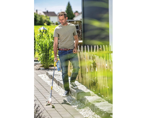 Muž používá plynový vypalovač plevele na dlážděné zahradní ploše k odstraňování plevele mezi dlaždicemi.