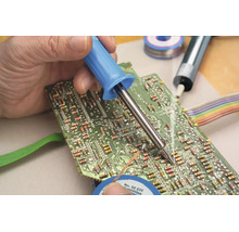 Ruka připájí elektronickou součástku na zelenou desku plošných spojů pomocí páječky.
