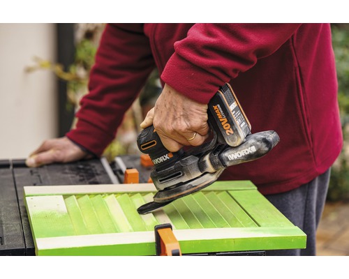 Řemeslník brousí zelené okenice pomocí akumulátorové multifunkční brusky Worx