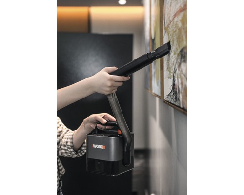 Osoba čistí obraz na zdi pomocí přenosného vysavače Worx.