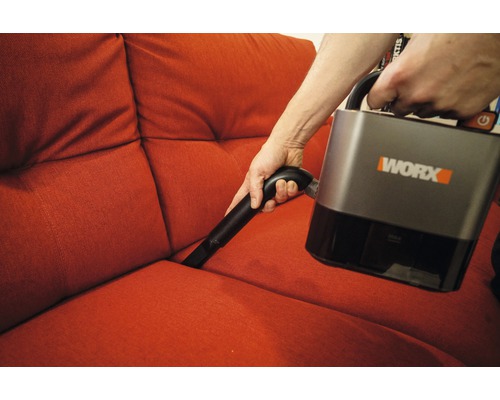 Osoba vysává pohovku akumulátorovým vysavačem Worx