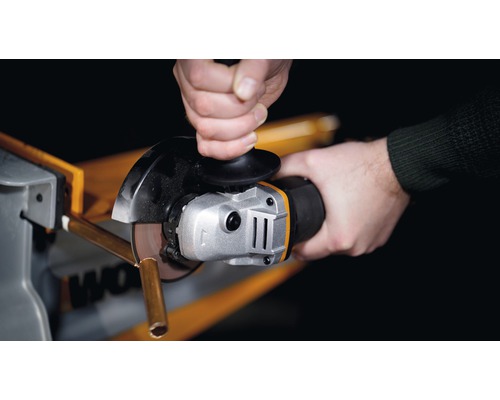 Detailní záběr osoby řezající kovovou trubku úhlovou bruskou.