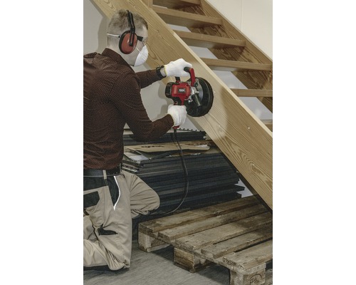 Řemeslník brousí dřevěné schodiště pomocí frézy na drážky do zdiva a používá přitom ochranné pomůcky.