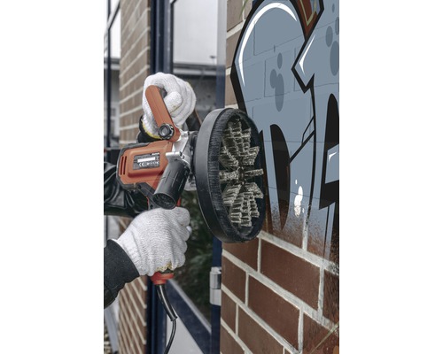 Osoba používá stroj na odstraňování graffiti na cihlové zdi.