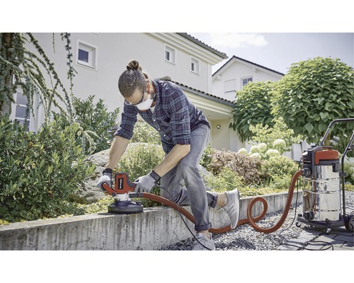 Muž brousí betonovou zeď na zahradě pomocí brusky na beton a vysavače.