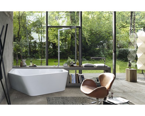 Světlá koupelna s vanou před prosklenou stěnou s výhledem do zahrady, křeslo a knihy