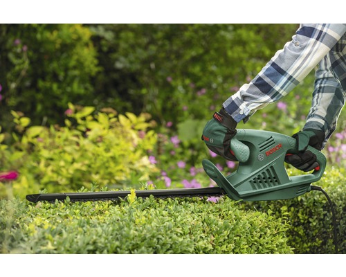 Osoba stříhá živý plot nůžkami na živý plot. Logo Bosch je viditelné.