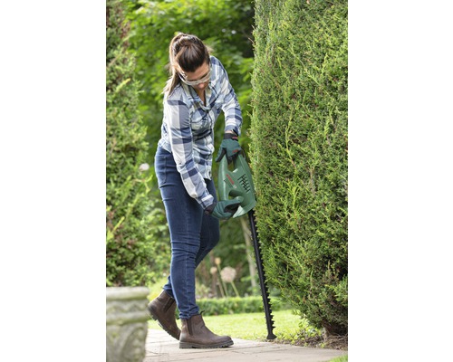 Žena stříhá živý plot nůžkami na živý plot Bosch na zahradě.