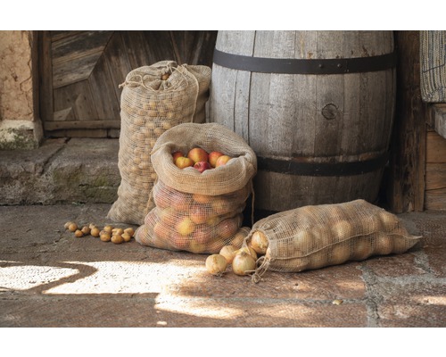Jutové pytle plněné jablky, cibulí a bramborami před dřevěným sudem