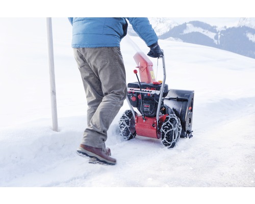 Osoba tlačí sněhovou frézu na zasněženém povrchu.