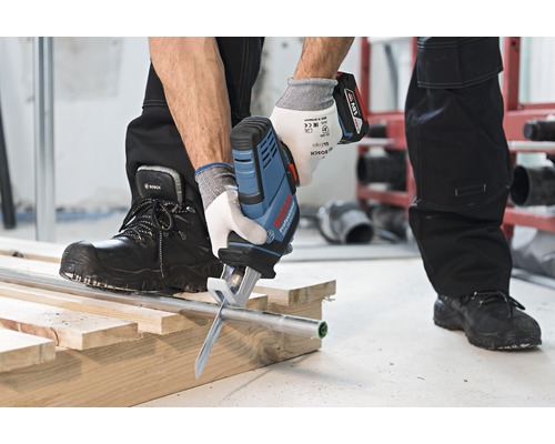 Akumulátorová pila řeže trubku na dřevěné konstrukci.