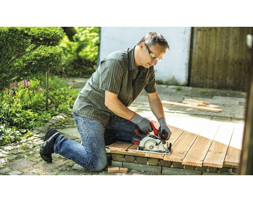 Muž řeže dřevo ruční okružní pilou na zahradě.