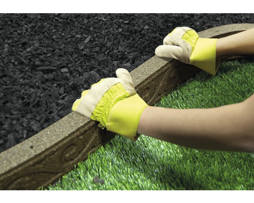 Osoba v rukavicích pokládá obrubník trávníku mezi gumový granulát a umělý trávník.