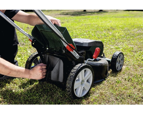 Osoba vyprazdňuje koš na trávu sekačky na trávníku.