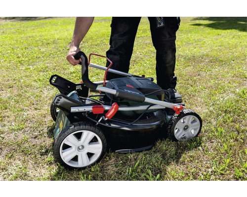 Osoba skládá sekačku na trávu s košem na trávu na trávníku.