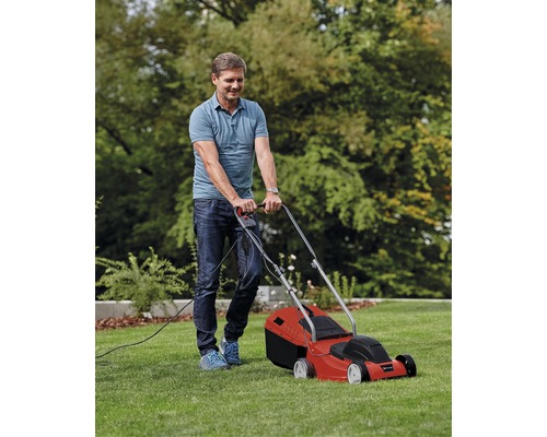 Muž seče trávník červenou elektrickou sekačkou na zahradě.