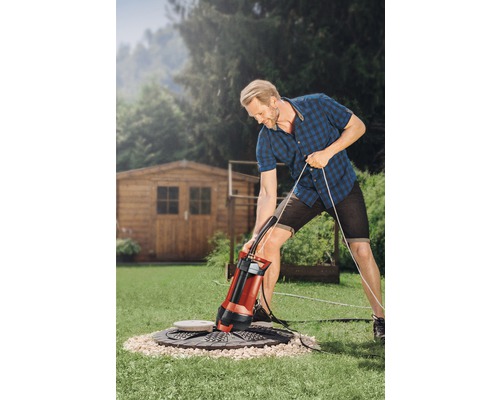 Muž obsluhuje ponorné čerpadlo v zahradě pro odvodnění šachty.