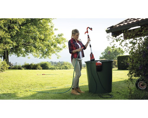 Žena obsluhuje teleskopický zahradní zavlažovač k zavlažování rostlin v zahradě.