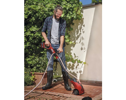 Muž používá akumulátorový kartáč na spáry v zahradě k odstraňování plevele mezi dlažebními kameny.