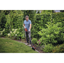 Muž stříhá okraje trávníku zastřihovačem trávníku na zahradě.