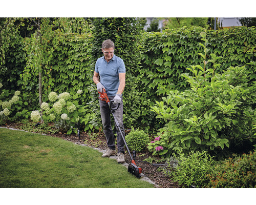 Muž stříhá okraje trávníku zastřihovačem trávníku na zahradě.