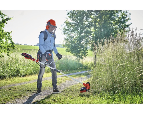 Muž stříhá trávu akumulátorovým vyžínačem na zahradě.