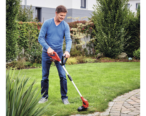 Muž stříhá okraje trávníku akumulátorovým vyžínačem na zahradě.