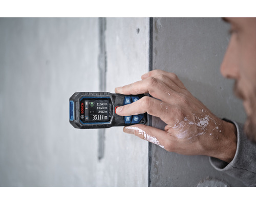 Osoba používá dálkoměr Bosch na stěně pro měření.