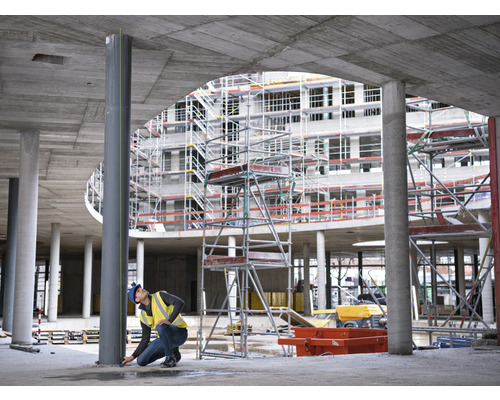 Stavební dělník měří ocelový sloup na staveništi.