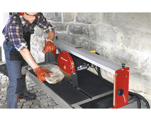 Muž s ochrannými brýlemi a chrániči sluchu obsluhuje řezačku dlaždic Einhell při řezání kamene