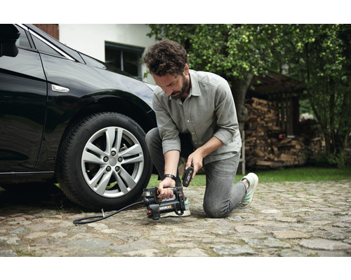 Muž plní pneumatiku auta přenosným kompresorem.