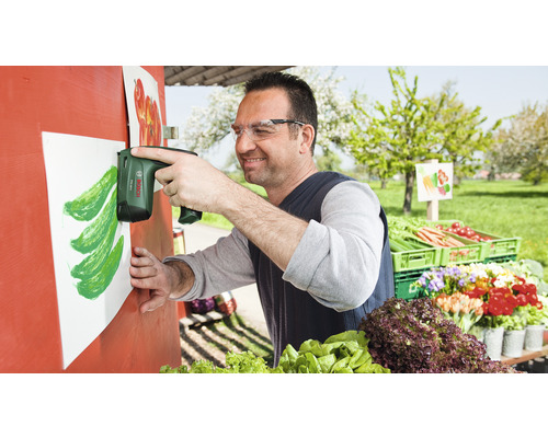 "Muž připevňuje elektrickou sešívačkou list papíru na dřevěnou konstrukci