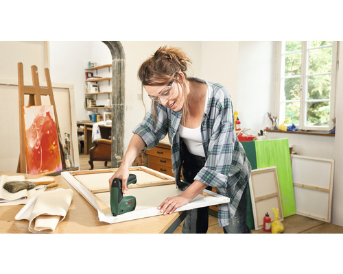 Žena používá elektrickou sešívačku k natahování plátna v jasném ateliéru.