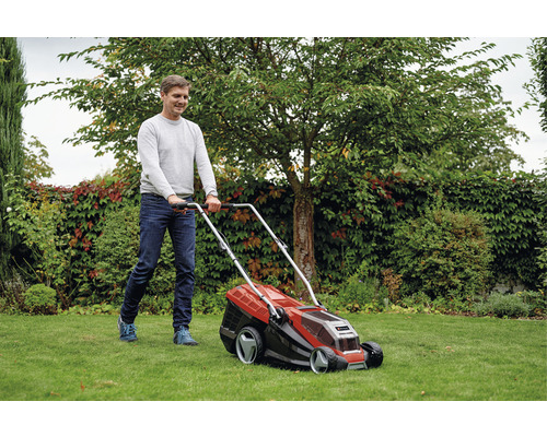 Muž seče trávník sekačkou na trávu na zahradě.