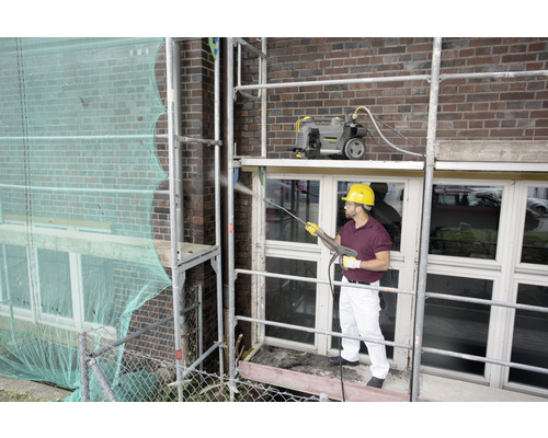 Muž na lešení čistí fasádu vysokotlakým čističem