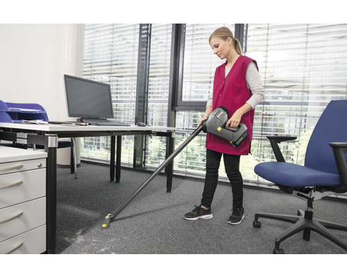 Žena vysává koberec v kanceláři akumulátorovým vysavačem.