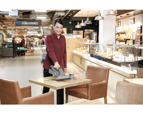 Žena čistí stůl s akumulátorovou okenní stěrkou v kavárně.