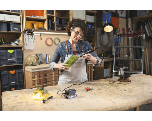 Žena vrtá otvor do skleněné láhve pomocí rotačního nástroje pro kutily v dílně.