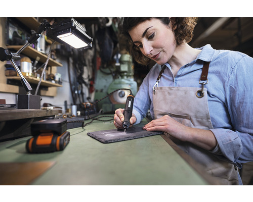 Žena gravíruje břidlicovou desku gravírovacím strojem na pracovním stole.