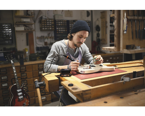 Muž pájí kytaru v dílně s páječkou