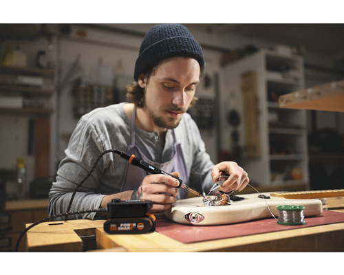 Muž pájí kytaru páječkou na pracovním stole.