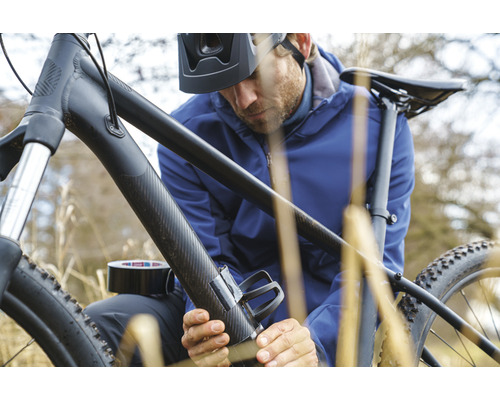 Muž připevňuje držák na láhev k jízdnímu kolu pomocí lepicí pásky.