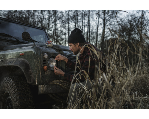Muž připevňuje lepicí pásku na světlomet terénního vozidla