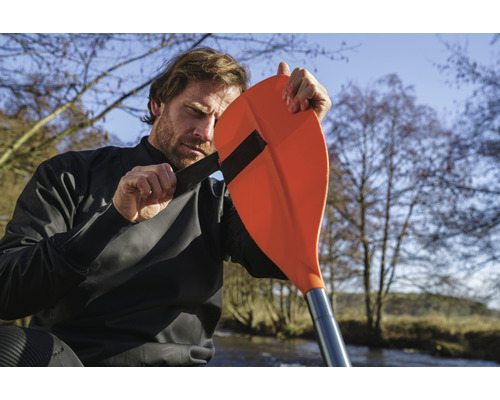 Muž upevňuje pádlo k suchému obleku na kajak pro outdoorové vodní sporty